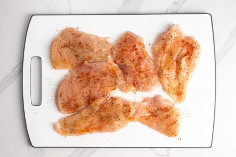 seasoned chicken cutlets on a white cutting board.