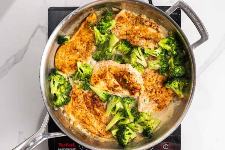 partially cooked chicken and broccoli added to a pan with cream sauce.