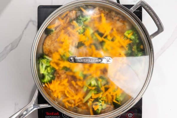 Cheese added to chicken and broccoli skillet. A lid is added so that the cheese will melt.