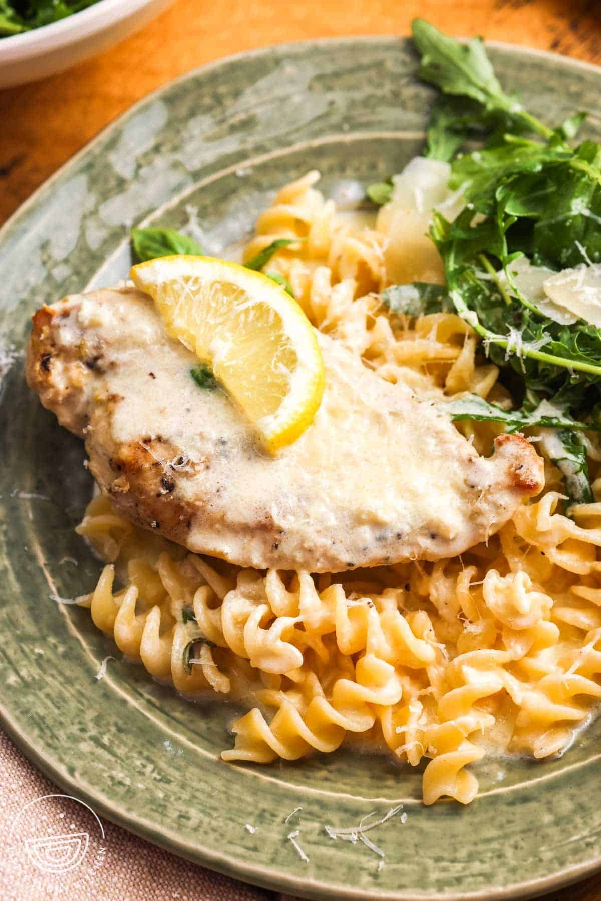 a green ceramic plate of rotini pasta with crockpot lemon chicken and a simple arugula salad.