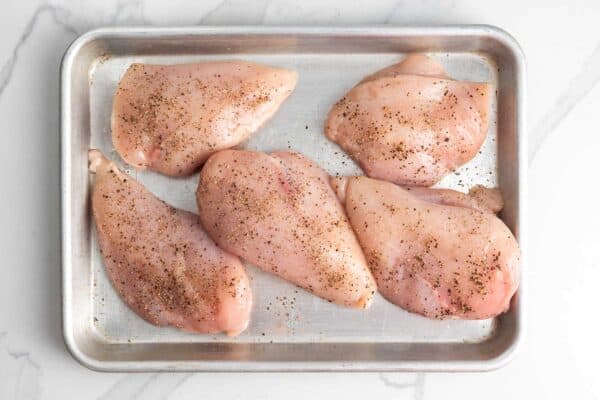 raw chicken breasts on a sheet pan seasoned with salt and pepper.