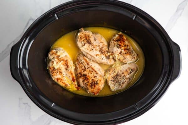 5 chicken breasts cooking in a crock pot in a lemon juice sauce with garlic