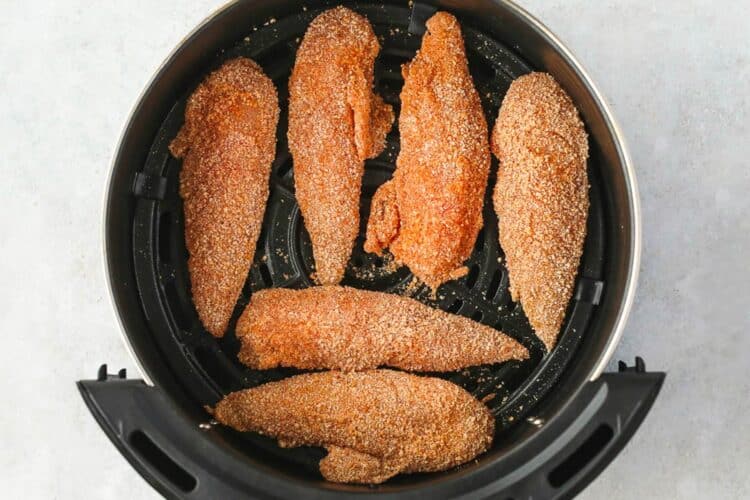 Breaded chicken tenders arranged in an air fryer basket before cooking.