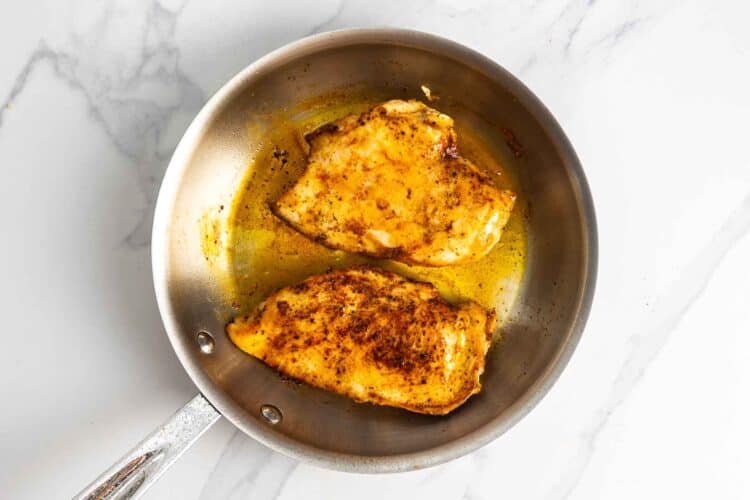 Seasoned chicken breasts cooking in a skillet with smoked paprika, salt, and black pepper.