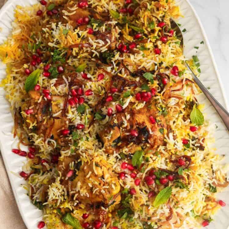 A platter of chicken biryani over rice, garnished with pomegranate arils and crispy fried onions.