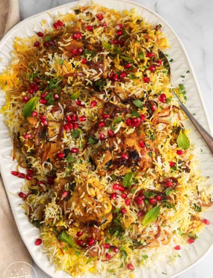 A platter of chicken biryani over rice, garnished with pomegranate arils and crispy fried onions.