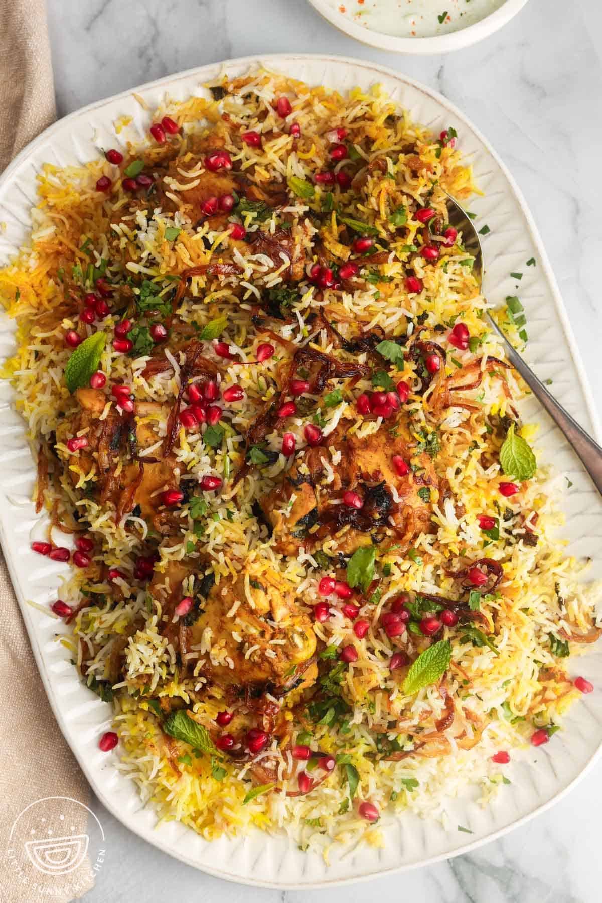 A platter of chicken biryani over rice, garnished with pomegranate arils and crispy fried onions.
