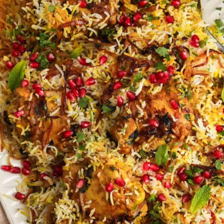 close up of A platter of chicken biryani over rice, garnished with pomegranate arils and crispy fried onions.