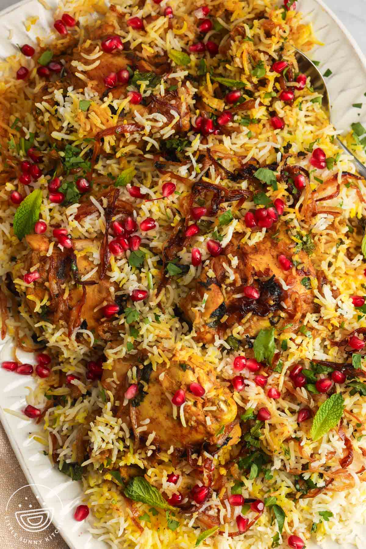 close up of A platter of chicken biryani over rice, garnished with pomegranate arils and crispy fried onions.