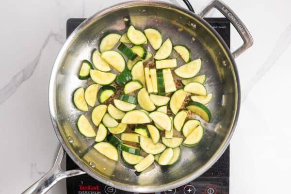 half moons of zucchini sauteed in a skillet.
