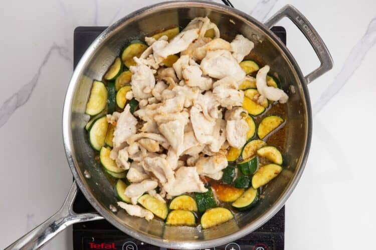 stir fried chicken added to a pan with zucchini and sauce.