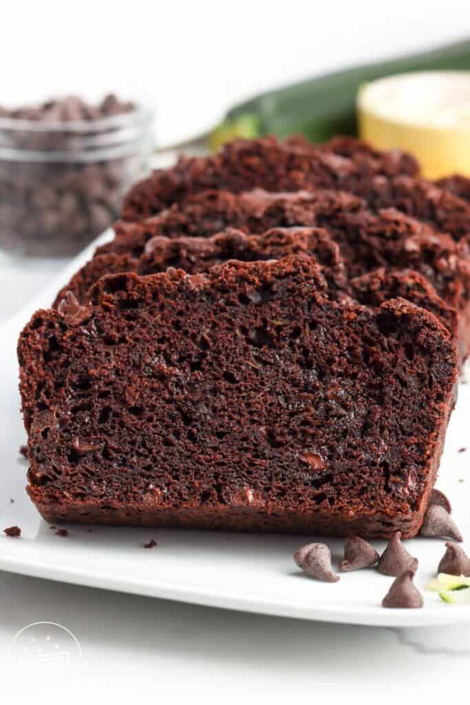 slices of double chocolate zucchini bread with chocolate chips on a white platter.