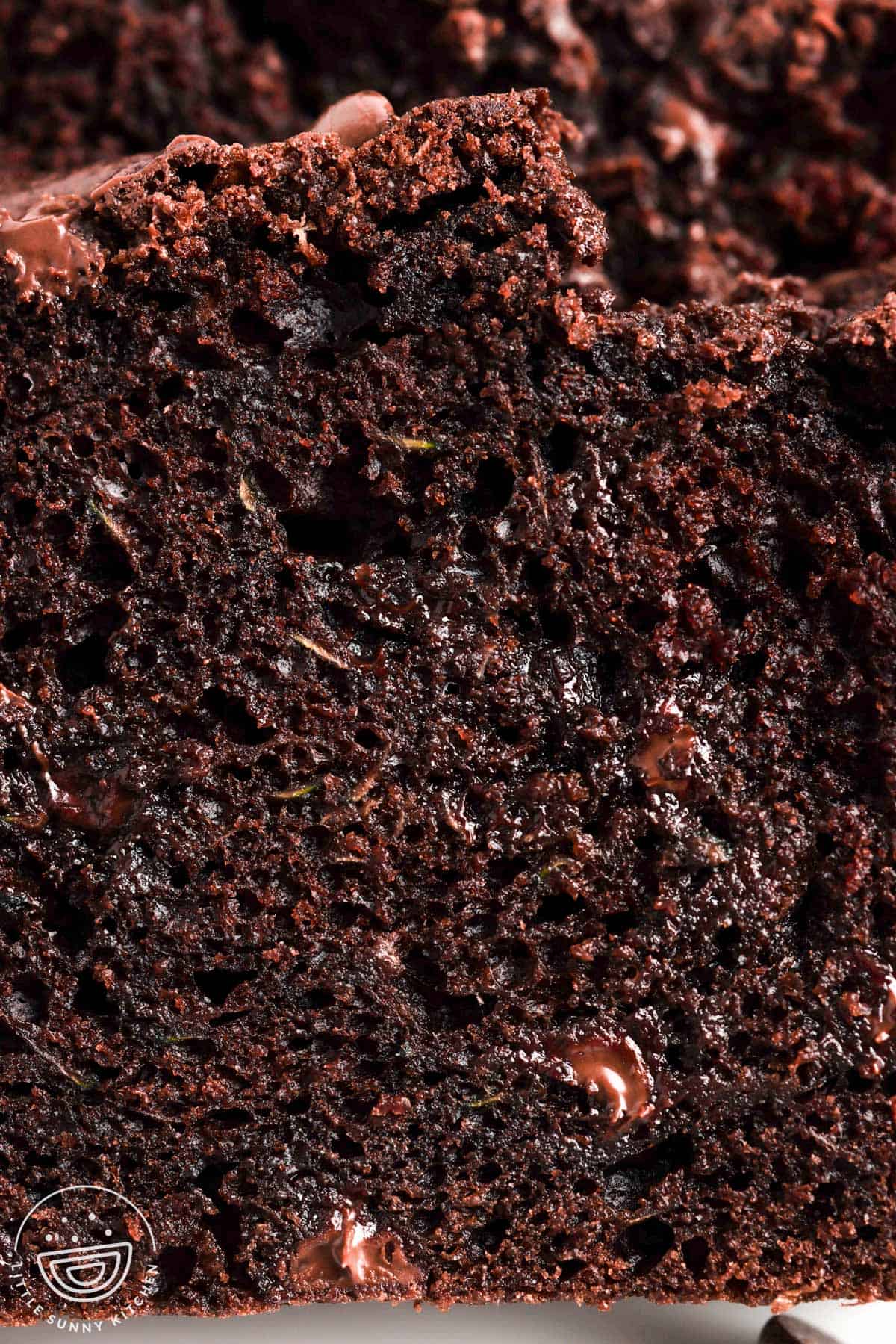 closeup of a slice of chocolate zucchini bread that shows the dark color, rich texture, chocolate chips, and very little green pieces.