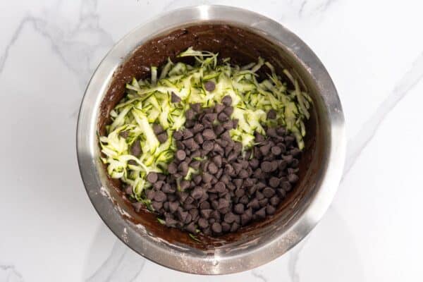 shredded zucchini and chocolate chips added to chocolate quick bread batter in a mixing bowl.