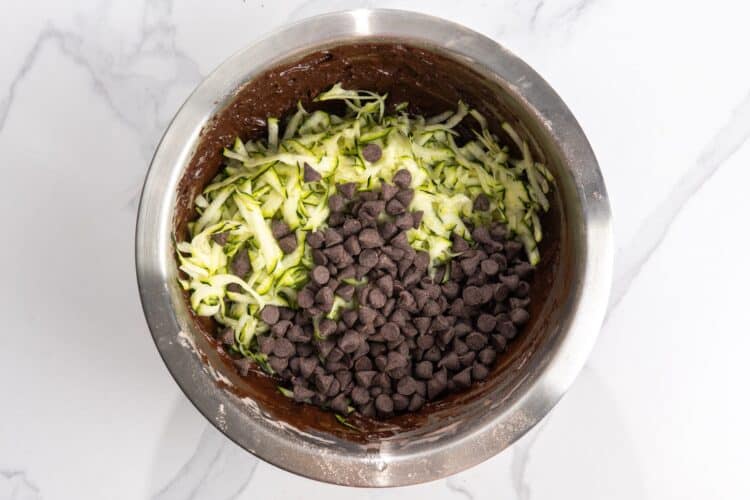shredded zucchini and chocolate chips added to chocolate quick bread batter in a mixing bowl.