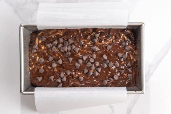 batter for chocolate zucchini bread in a parchment lined loaf pan, topped with chocolate chips