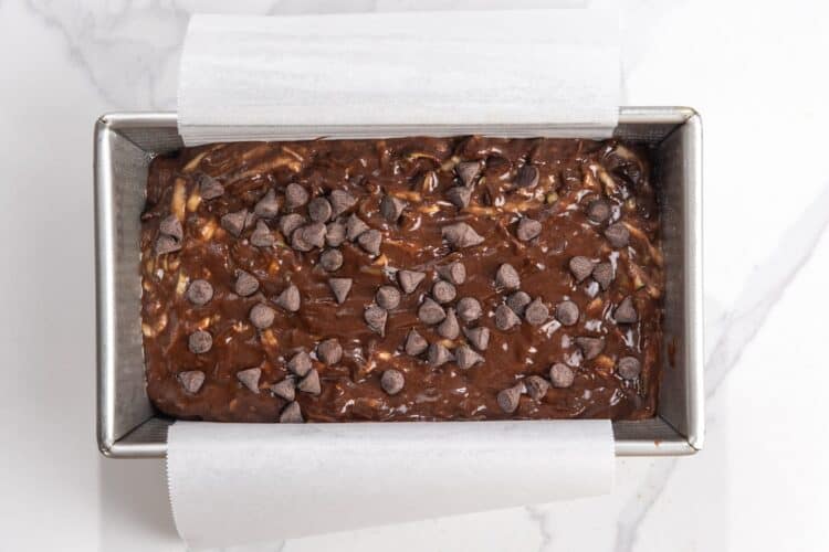 batter for chocolate zucchini bread in a parchment lined loaf pan, topped with chocolate chips