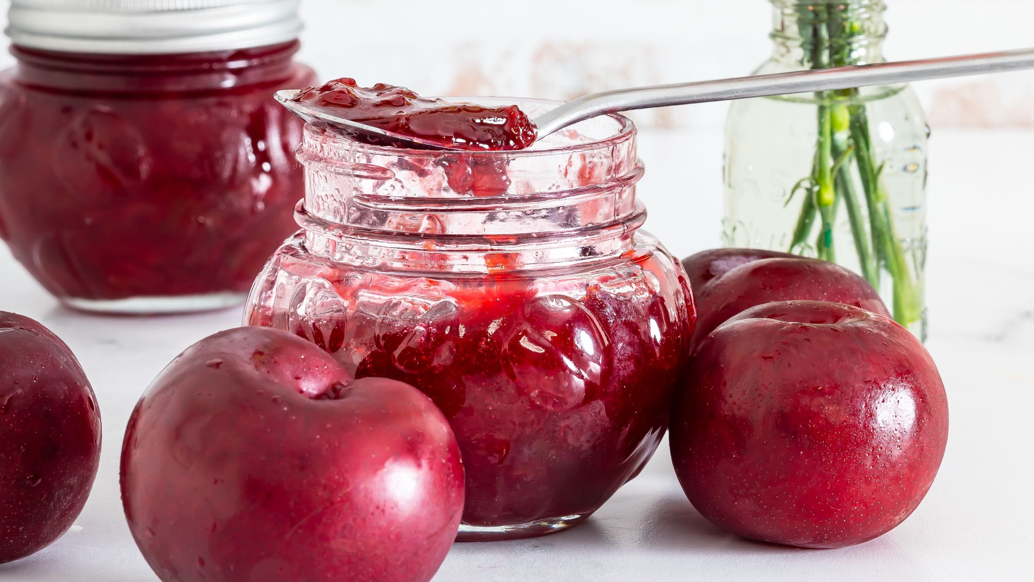 Homemade plum jam in a glass jar with fresh red plums and a spoonful of jam