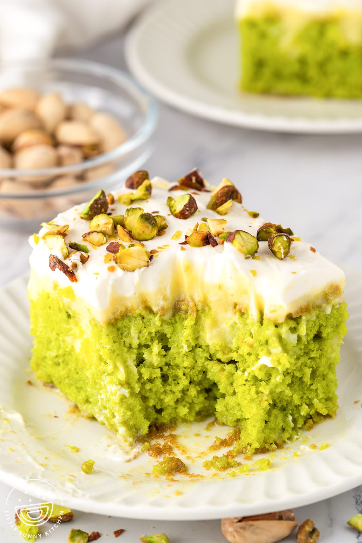 Partially eaten slice of pistachio poke cake with moist green cake, creamy layers, and chopped pistachios