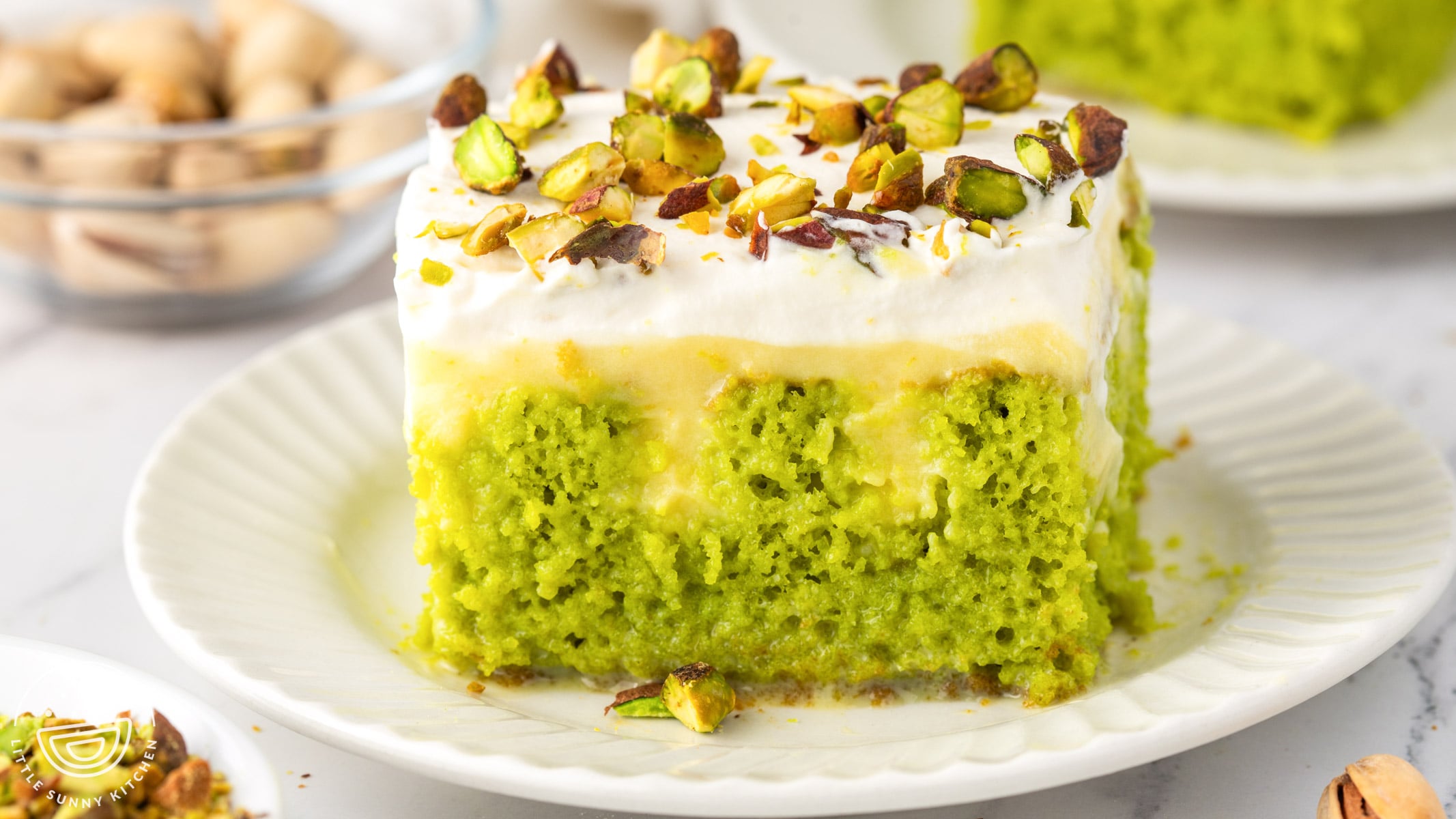 Slice of pistachio poke cake with vanilla pudding, whipped cream, and chopped pistachios