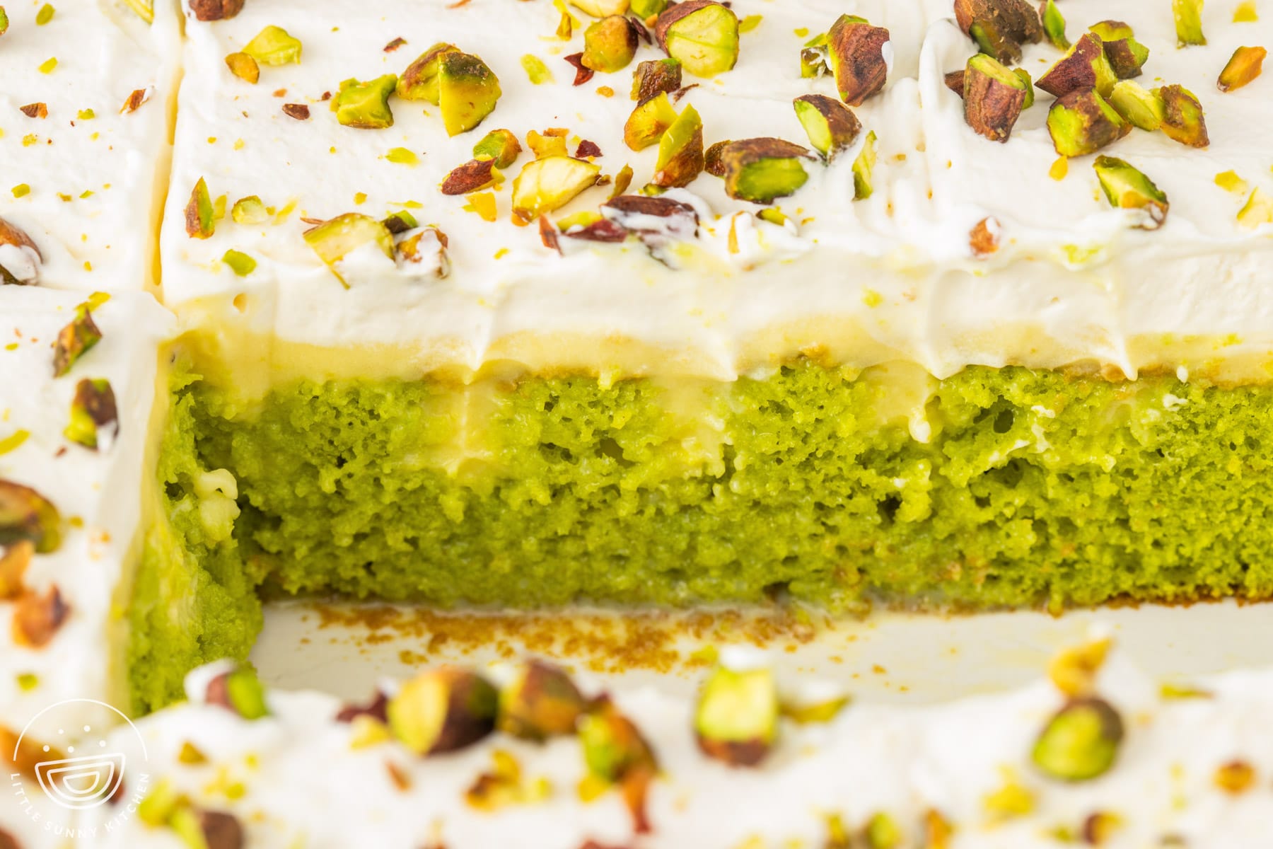 Close up of pistachio poke cake showing the condensed milk soaked cake, vanilla pudding, whipped cream, and chopped pistachios