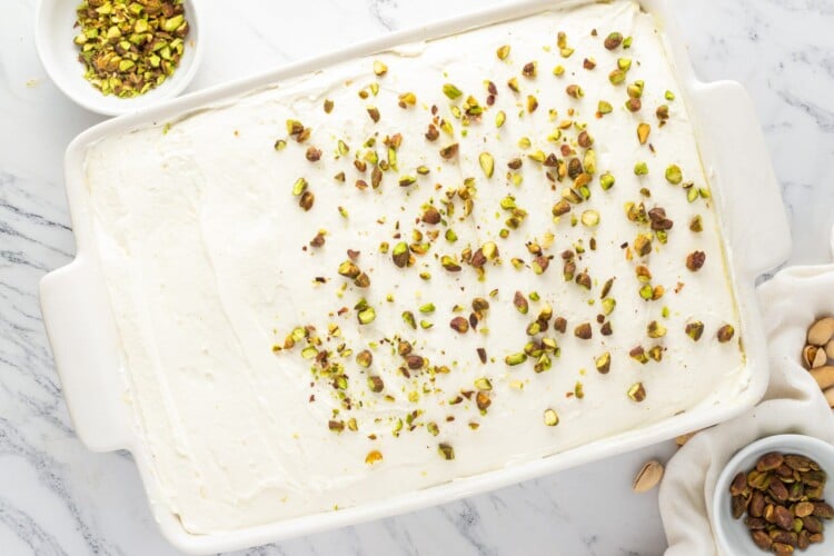 Pistachio poke cake topped with whipped cream and chopped roasted pistachios in a 9 by 13 inch baking dish