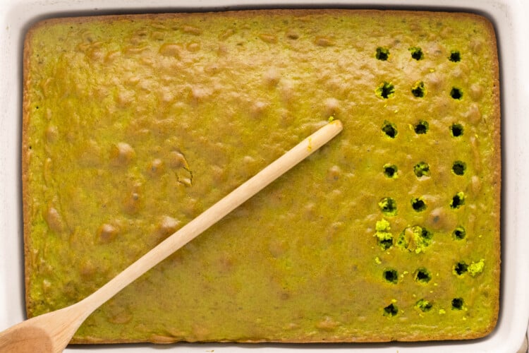 Poking evenly spaced holes in the baked pistachio cake with a wooden spoon handle