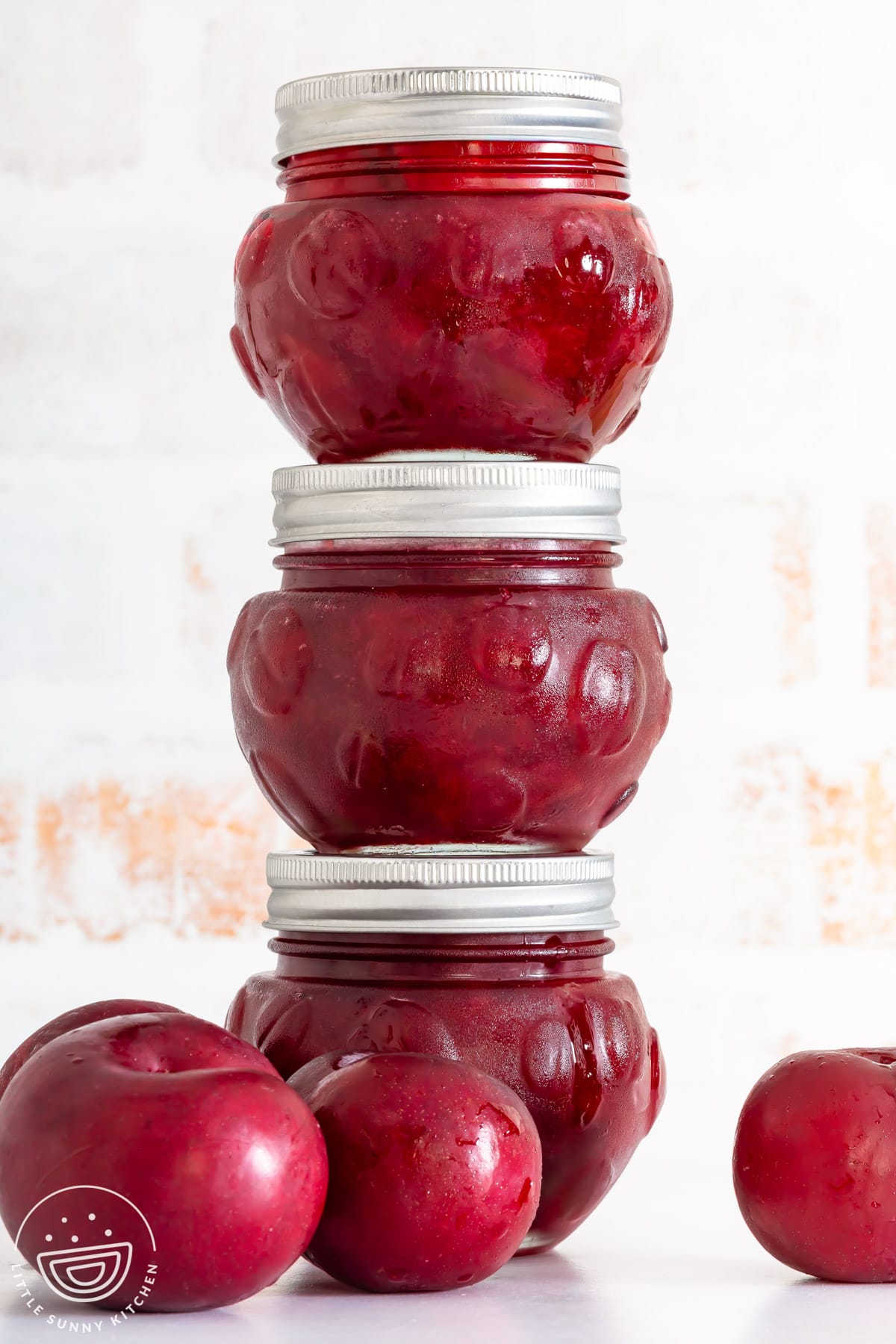Three jars of homemade plum jam stacked with fresh red plums.