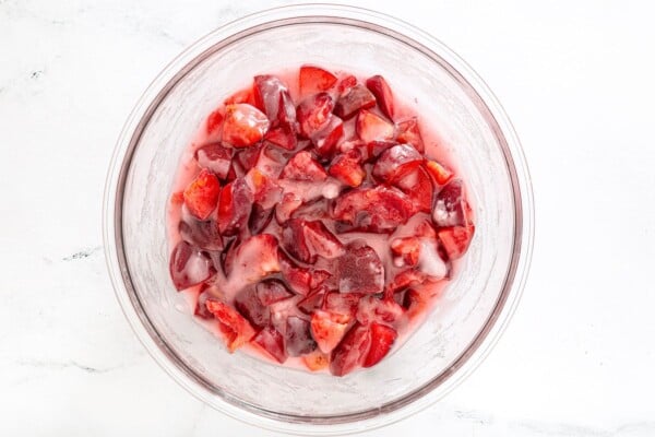 Chopped plums mixed with sugar and lemon juice in a glass bowl