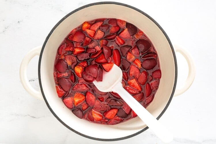 Plum mixture cooking in a heavy-bottomed pot with a spatula