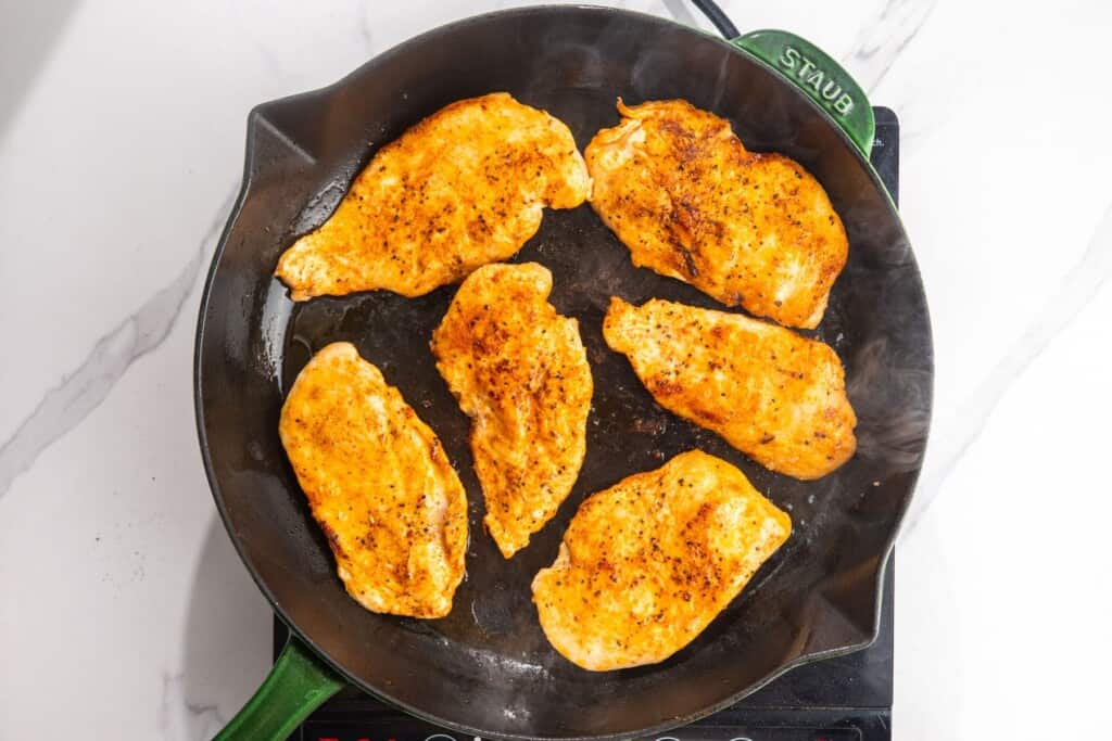 Seasoned chicken cutlets searing until golden brown in a cast-iron skillet.