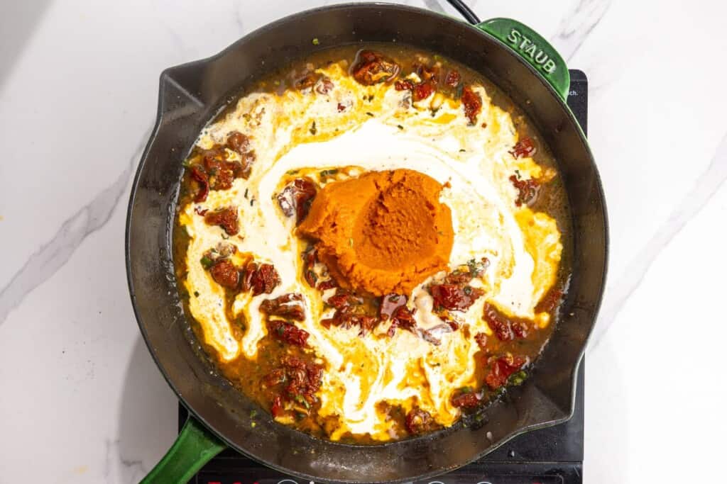 Pumpkin puree and heavy cream added to a skillet with sun-dried tomatoes, garlic, and sage.