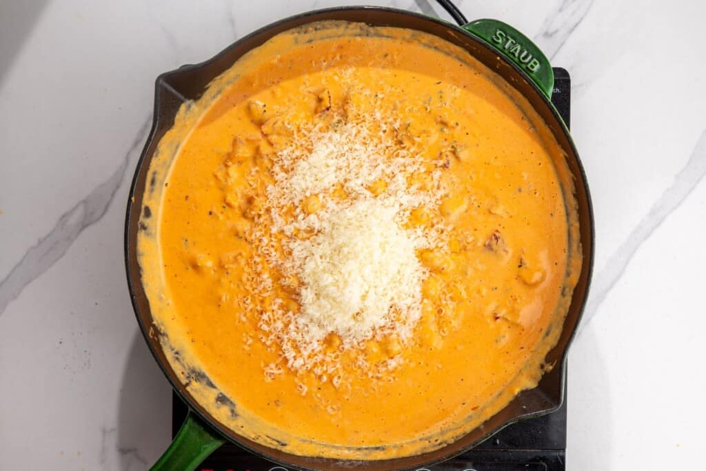 Freshly grated Parmesan added to the smooth pumpkin cream sauce in a skillet.