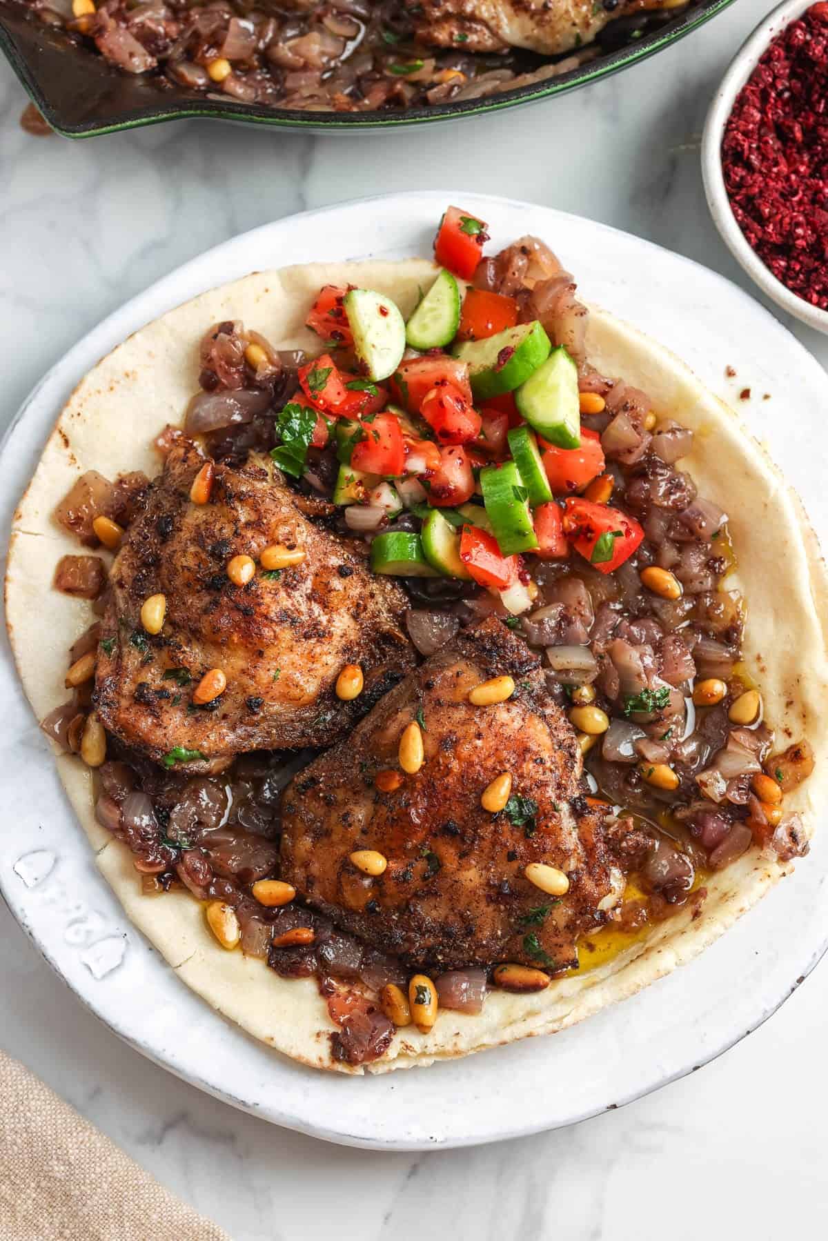 Sumac chicken thighs served over pita with onions, pine nuts, and chopped tomato cucumber salad.
