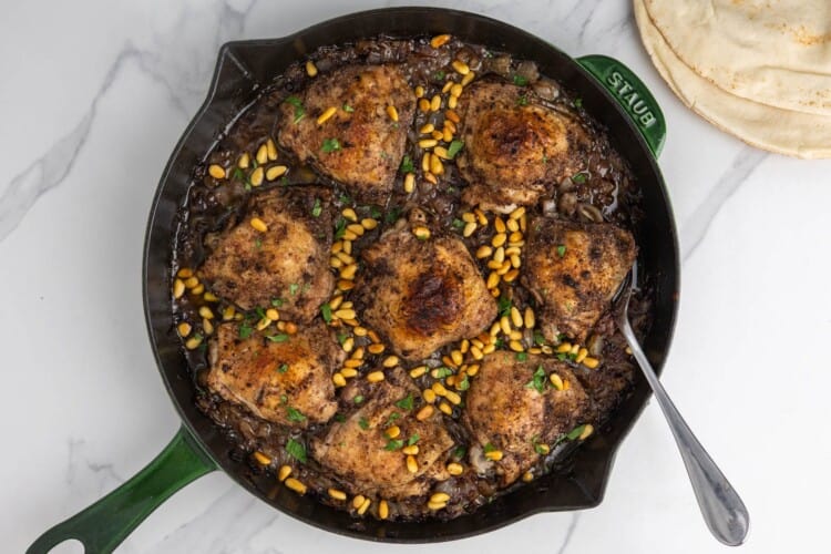 Baked sumac chicken thighs with onions, pine nuts, and parsley in a cast-iron skillet.