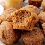 a pile of applesauce muffins topped with cinnamon sugar. One has a bite taken out to show the fluffy texture.