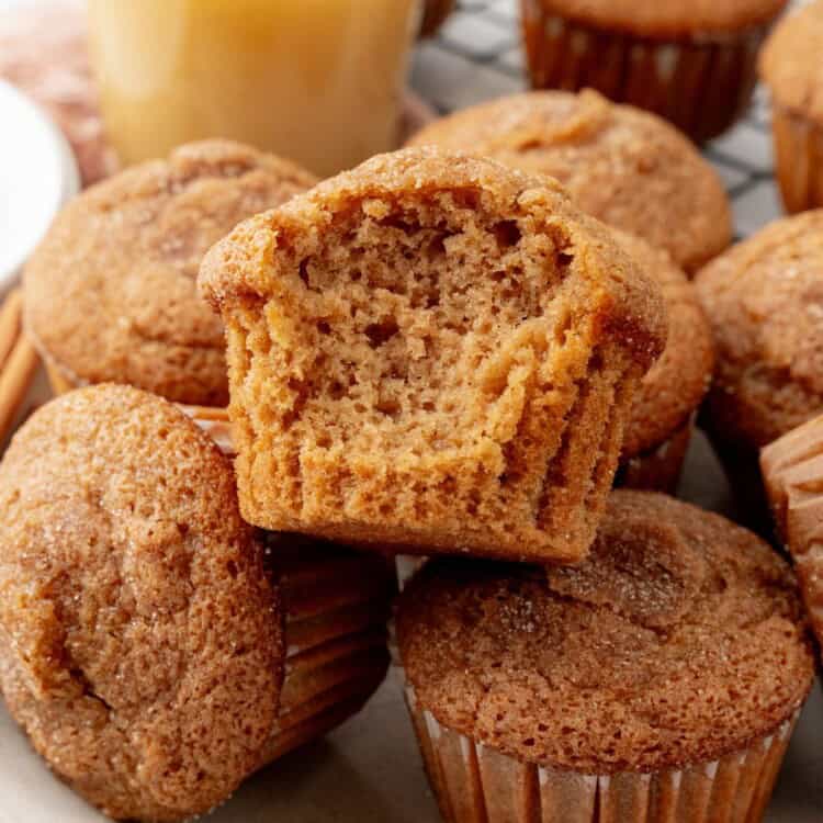 a pile of applesauce muffins topped with cinnamon sugar. One has a bite taken out to show the fluffy texture.