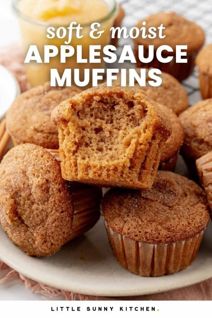a pile of applesauce muffins topped with cinnamon sugar on a plate. One has a bite taken out to show the fluffy texture. Text overlay says "soft and moist applesauce muffins"