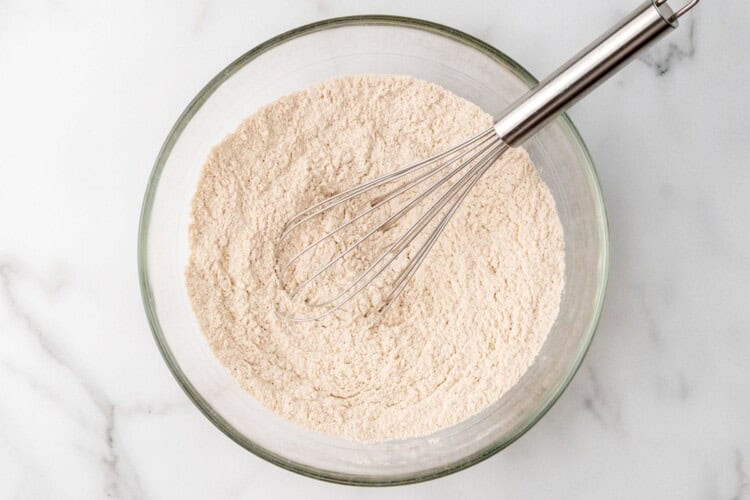 a bowl of flour mixed with cinnamon and leaveners with a whisk.