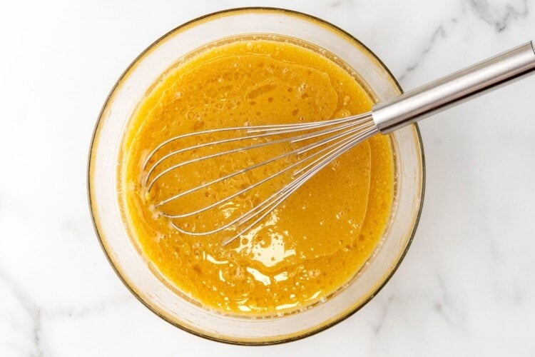 a mixing bowl of applesauce mixed with oil and sugar with a metal whisk.