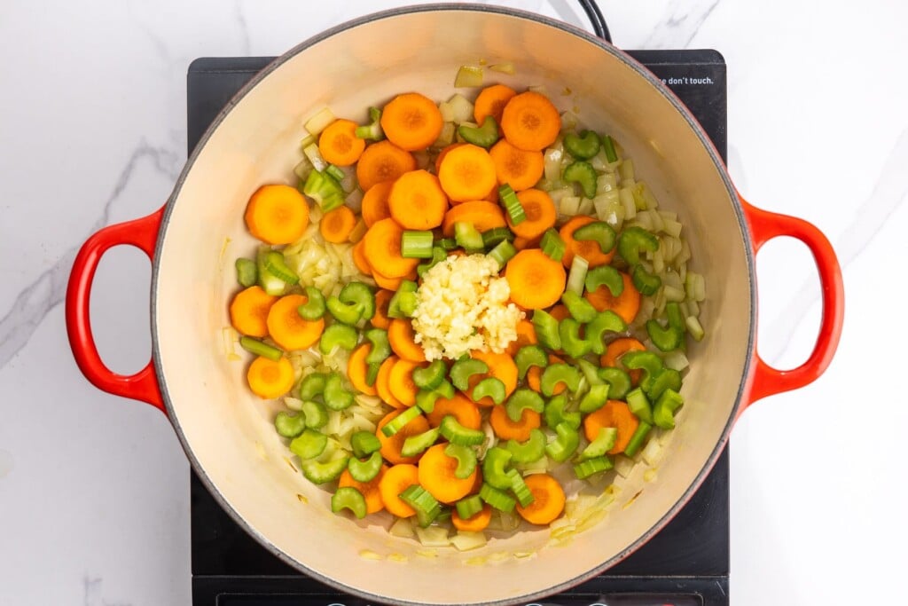 sliced carrots, sliced celery, and minced garlic added to a dutch oven with sauteed onions.
