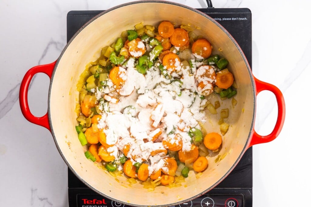 all purpose flour added to a pot of sauteed vegetables.