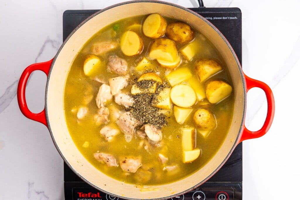 chicken stewing in a dutch oven with potatoes, broth, and seasonings.