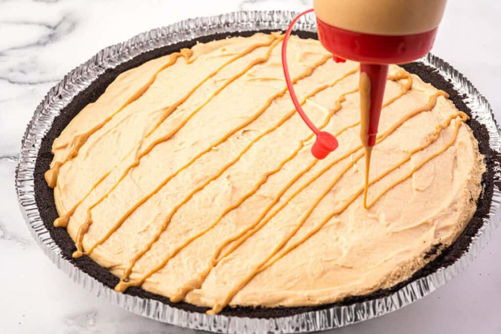 peanut butter drizzled over a peanut butter pie with a squeeze bottle