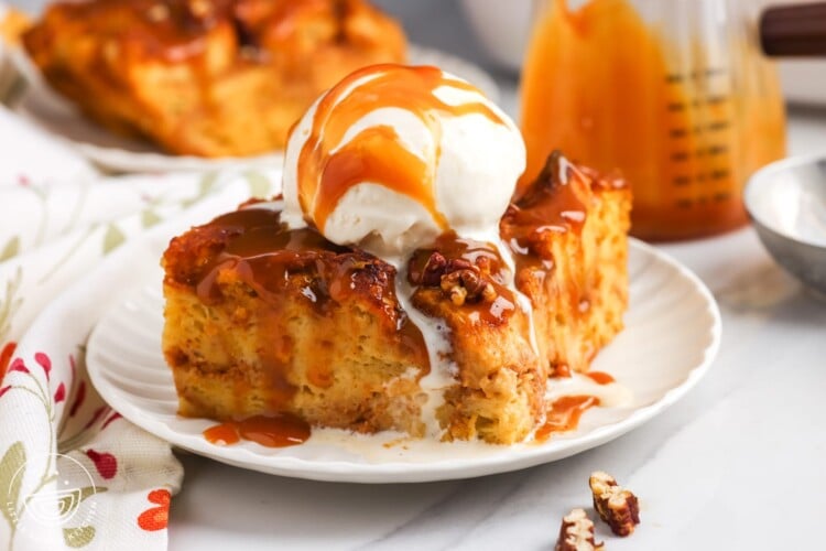 side view of a slice of creamy pumpkin bread pudding topped with chopped nuts, ice cream, and caramel sauce.