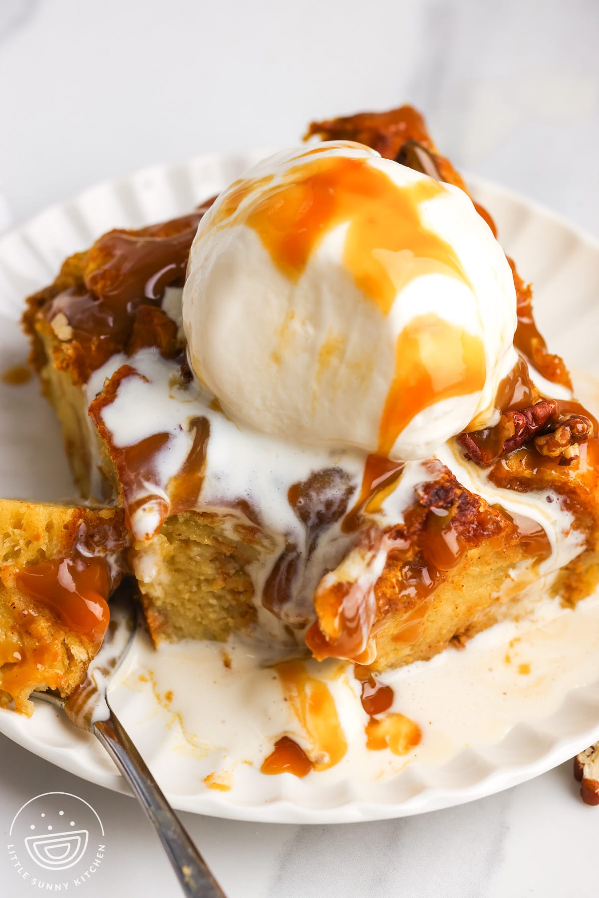a square piece of pumpkin bread pudding on a plate, topped with melty vanilla ice cream and caramel sauce.