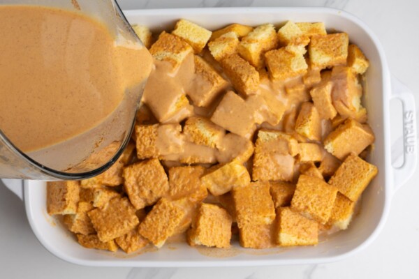 pumpkin custard poured over a pan of cubed brioche bread.