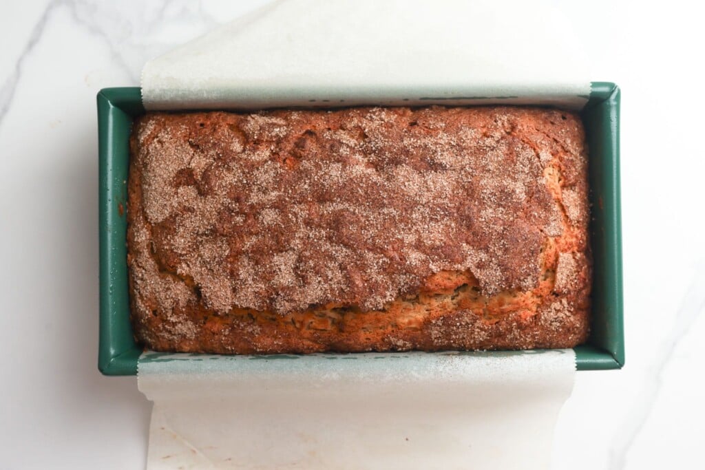 Baked apple bread with a deep golden brown top in a green loaf pan.