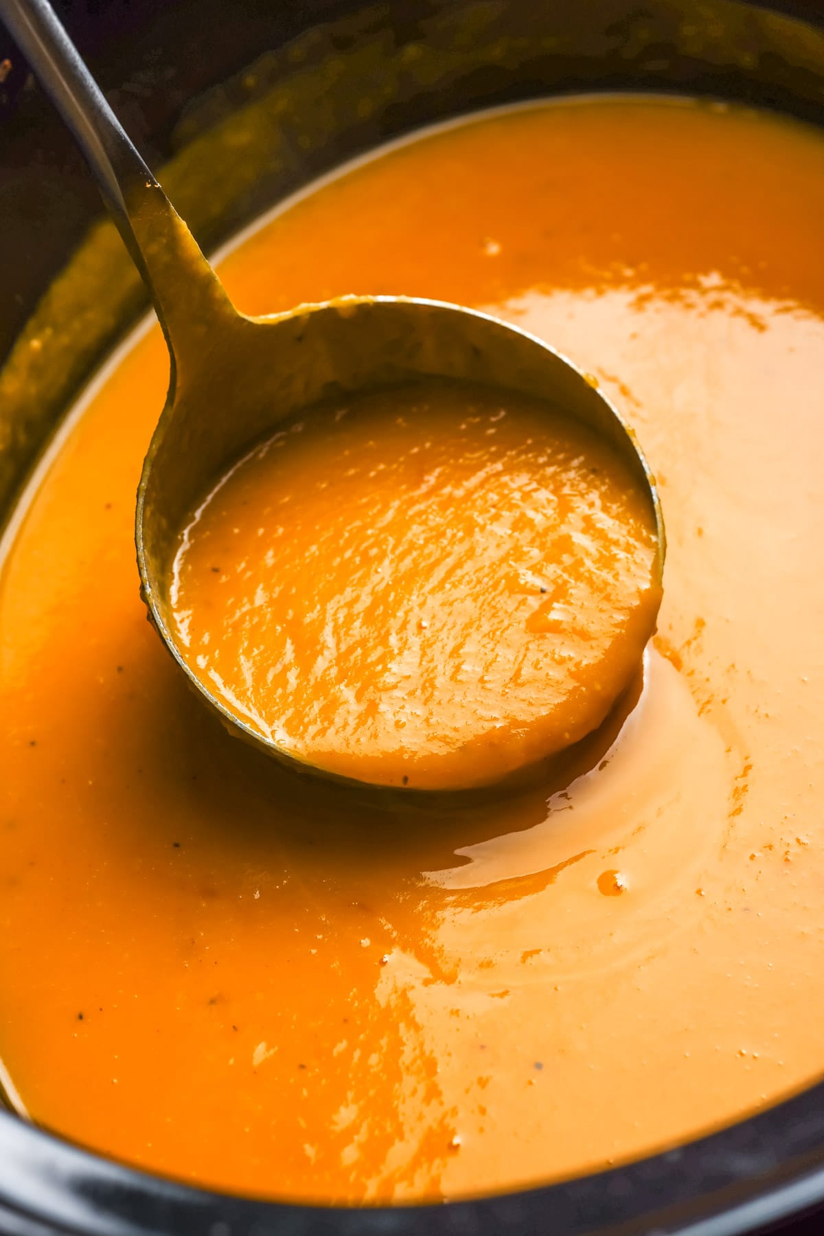 A ladle lifting smooth butternut squash apple soup out of a slow cooker.