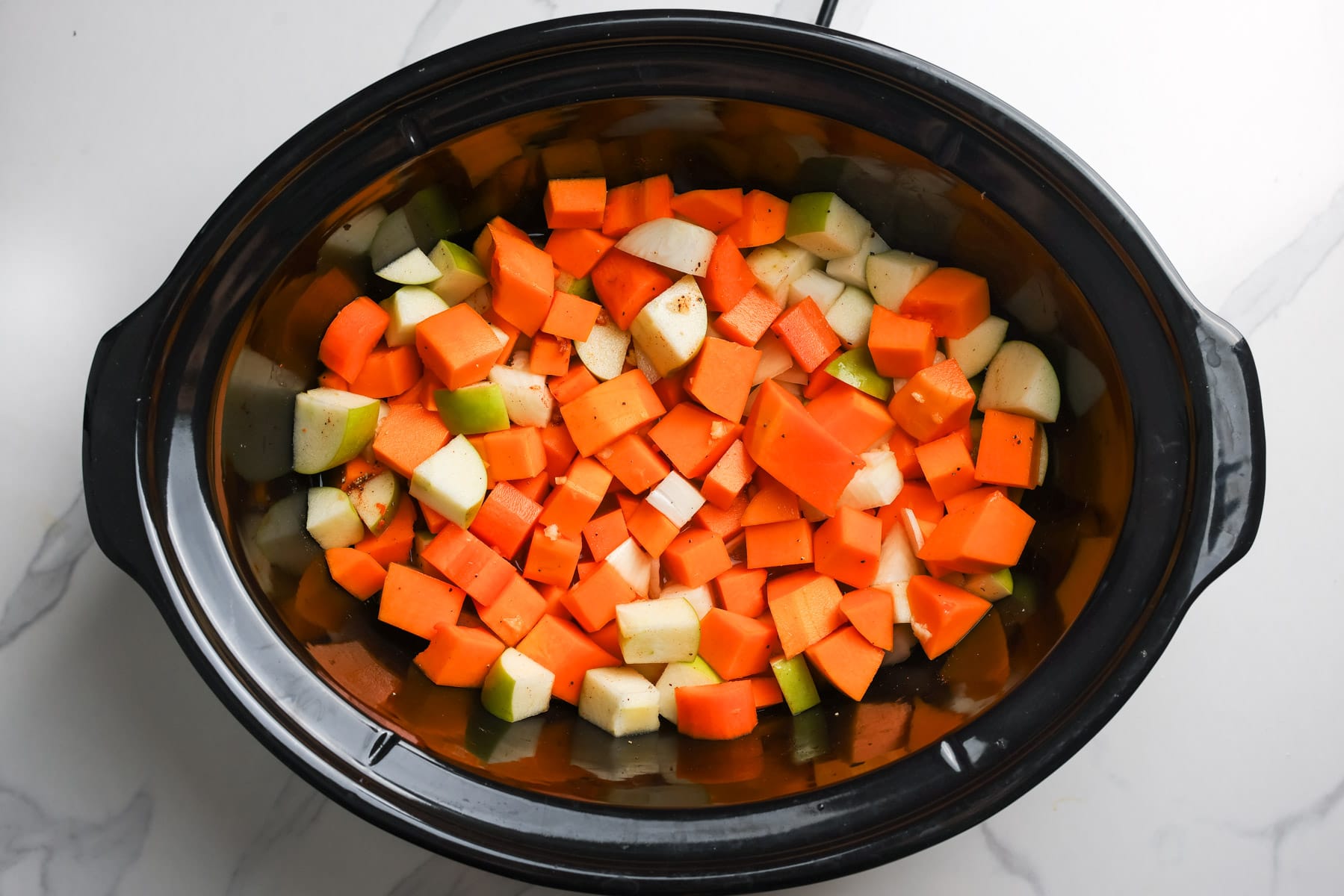 Cubed butternut squash, diced Granny Smith apples, carrot, and onion in a slow cooker before cooking.